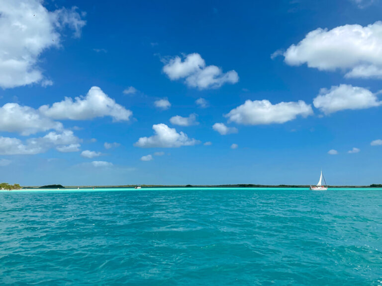 Small sailboat on brilliant blue water against a blue sky with puffy white clouds.