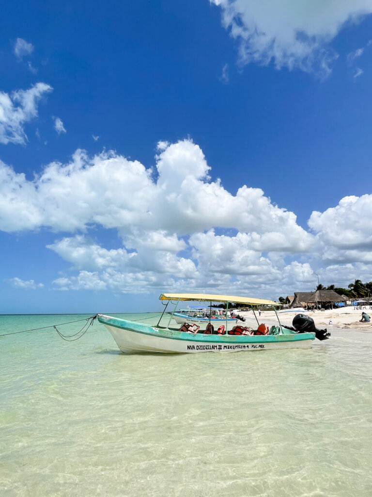 Blue and white boat floating in shallow turquoise waters against a blue sky with puffy clouds.