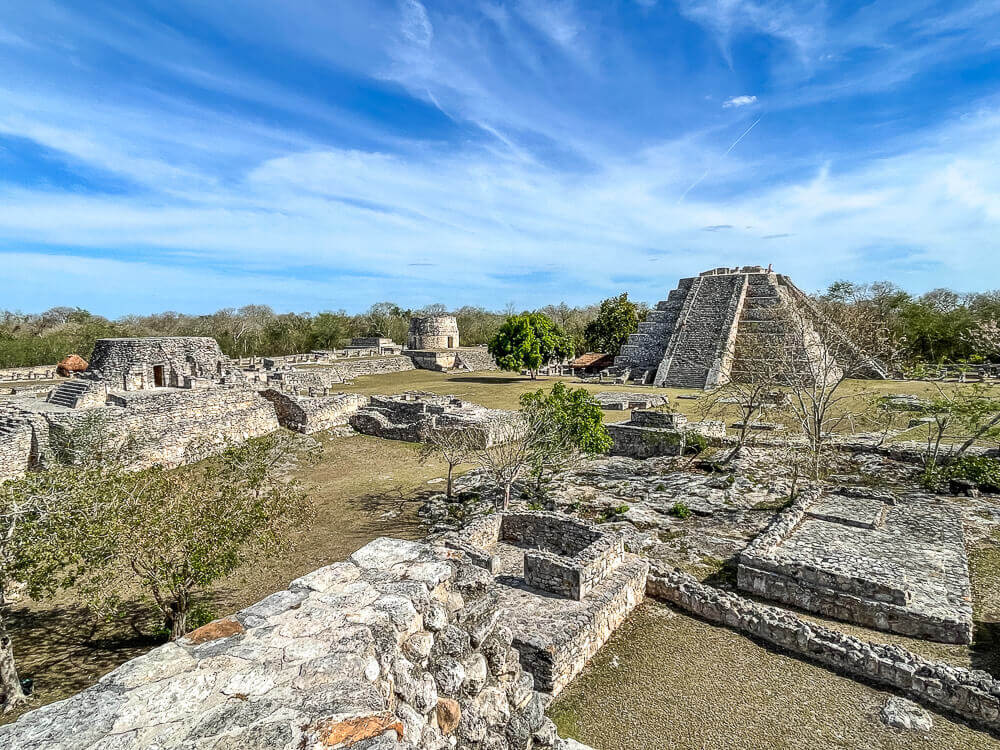 A Mayan pyramid and other buildings at an archeological site, against a blue sky with wispy clouds