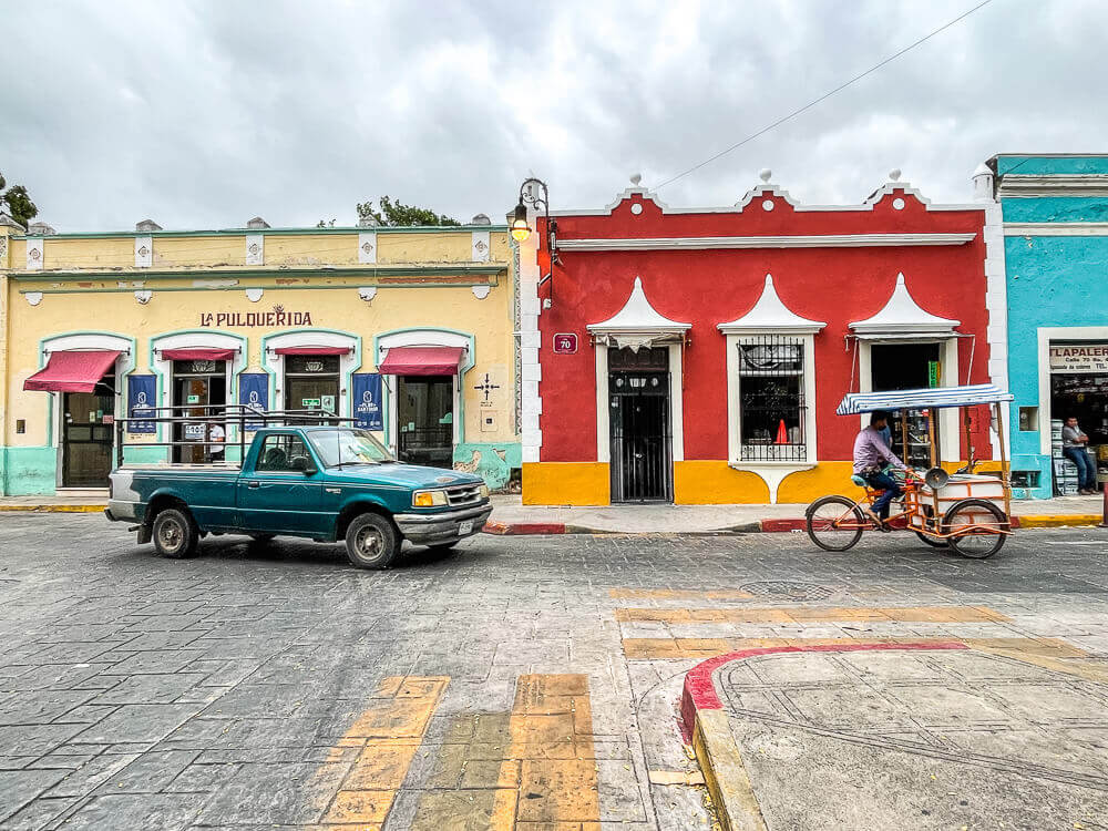 pickup truck and cargo bicycle passing in front of colorful one-story buildings