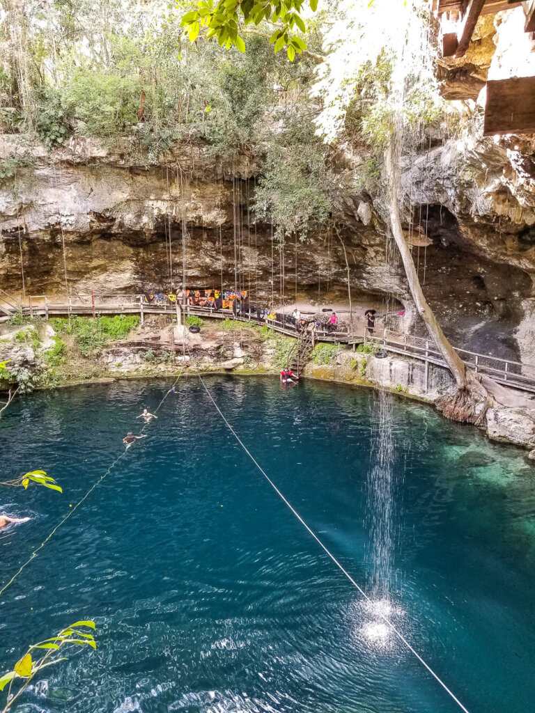 Blue water of a cenote (limestone pool) with people waiting to get in