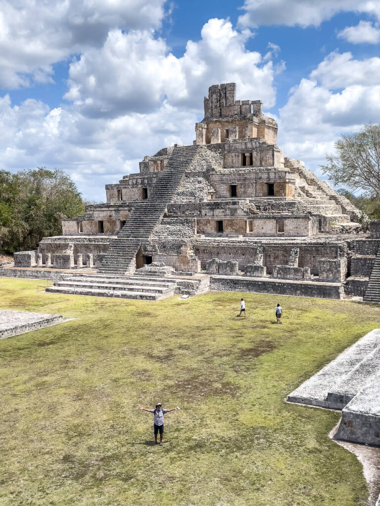 Ancient stone pyramid with five levels, with  a grassy plaza in the foreground and a blue sky with puffy clouds