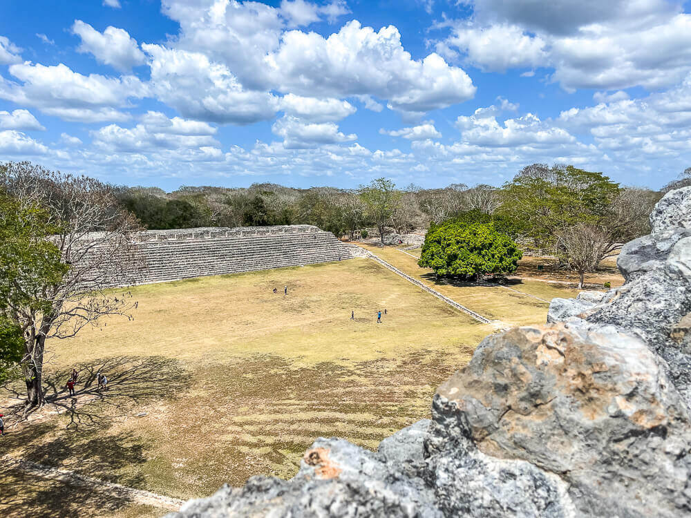 Ancient stone structures on a grassy plaza, against a blue sky with puffy clouds