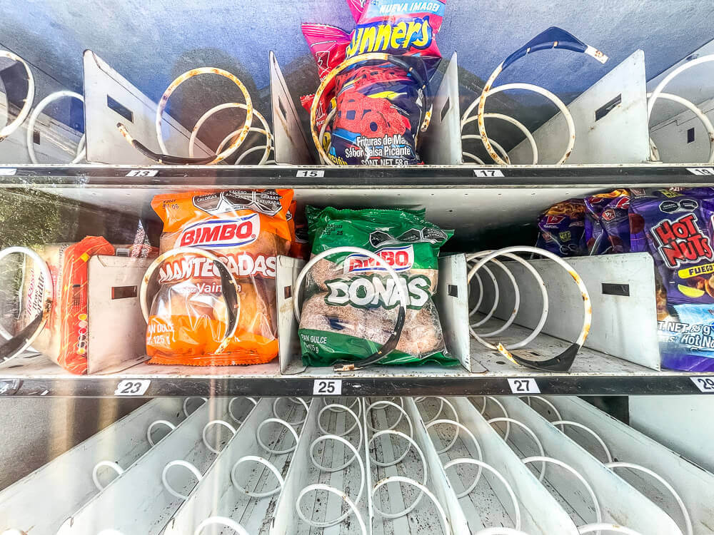 Inside of a vending machine, with mostly empty spaces and a few bags of donuts and chips