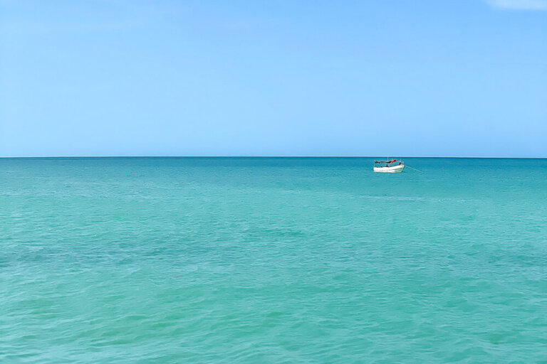 small white boat floating on turquoise sea