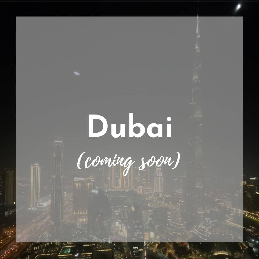 Foreground: a transparent grey box with Dubai (coming soon) in white text Background photo: night picture with dark sky and tall skyscrapers lit up