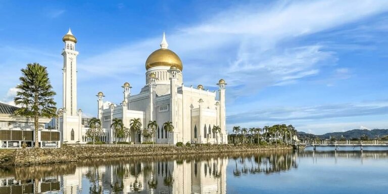 white mosque with gold dome is reflected in clear blue water below