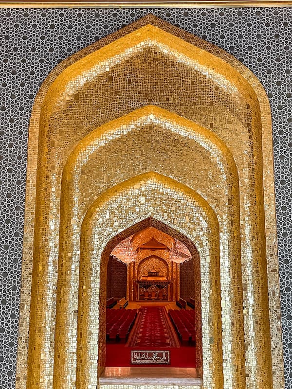 A golden archway framed by intricate blue and white tile, leading to a dark room with red chairs and carpet.