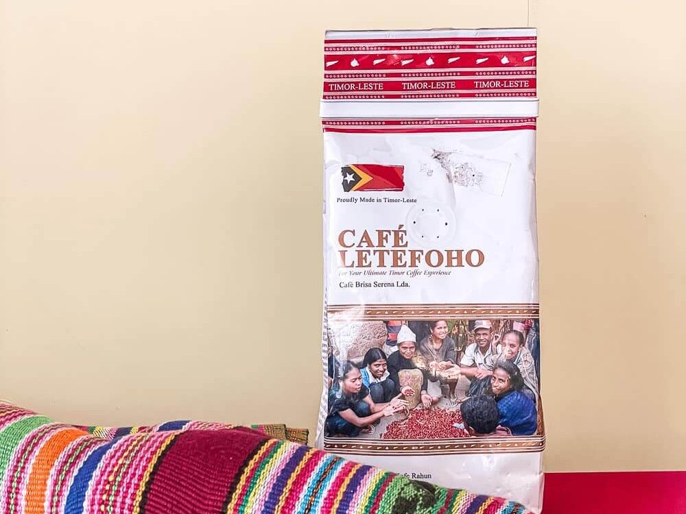 A red and white package with red writing and a photo sits on a red shelf. There is a colorful striped fabric rumpled in front of the bag.