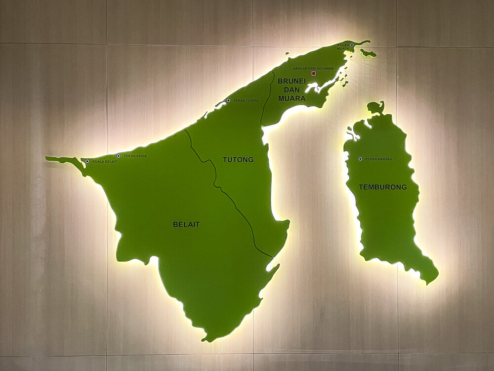 A green map of Brunei is backlit against a beige wall.