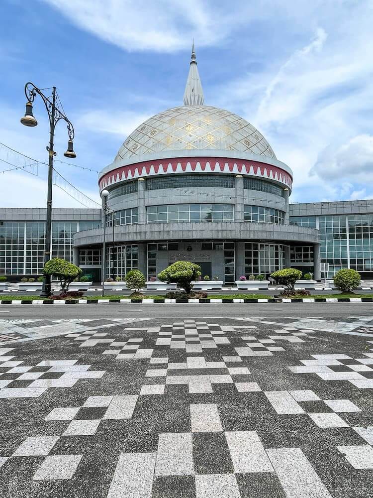 A patterned walkway leads to a large building with a silver-grey domed roof