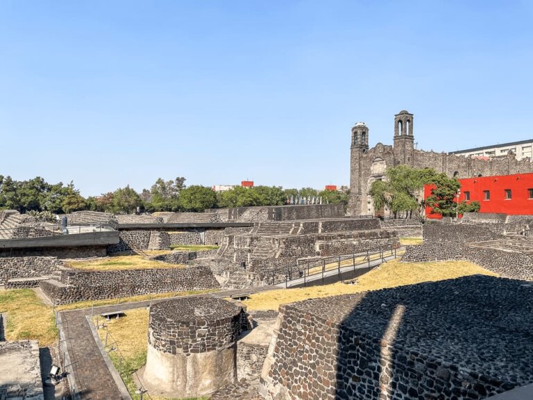 A large site with ancient pyramid-like structures built with volcanic stone. A church is in the background.