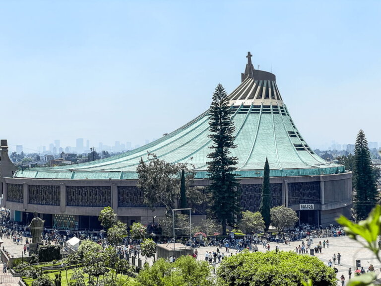 A large building with a light blue curved roof leading up to a cross