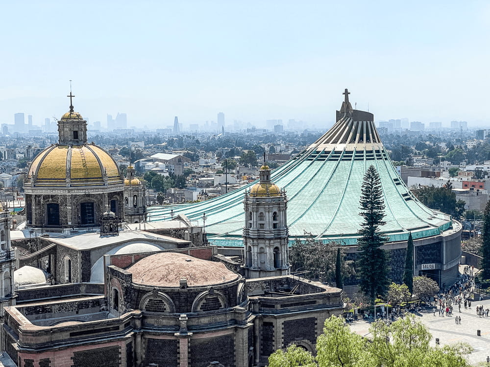 On the right, a large building with a light blue curved roof leading up to a cross. On the left, an older gold cupola of a church building.