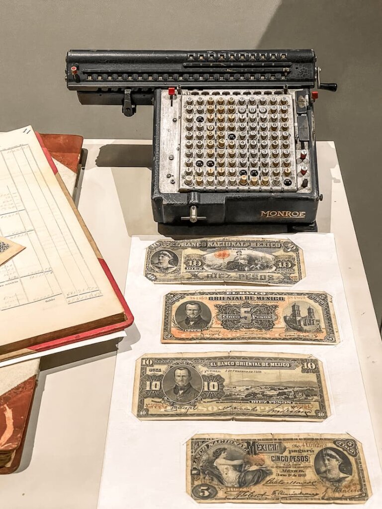 Objects on a table, including a black machine with number buttons and old currency.