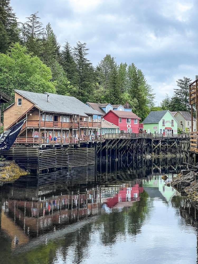 A row of colorful wooden houses on stilts line the edge of a calm creek. 