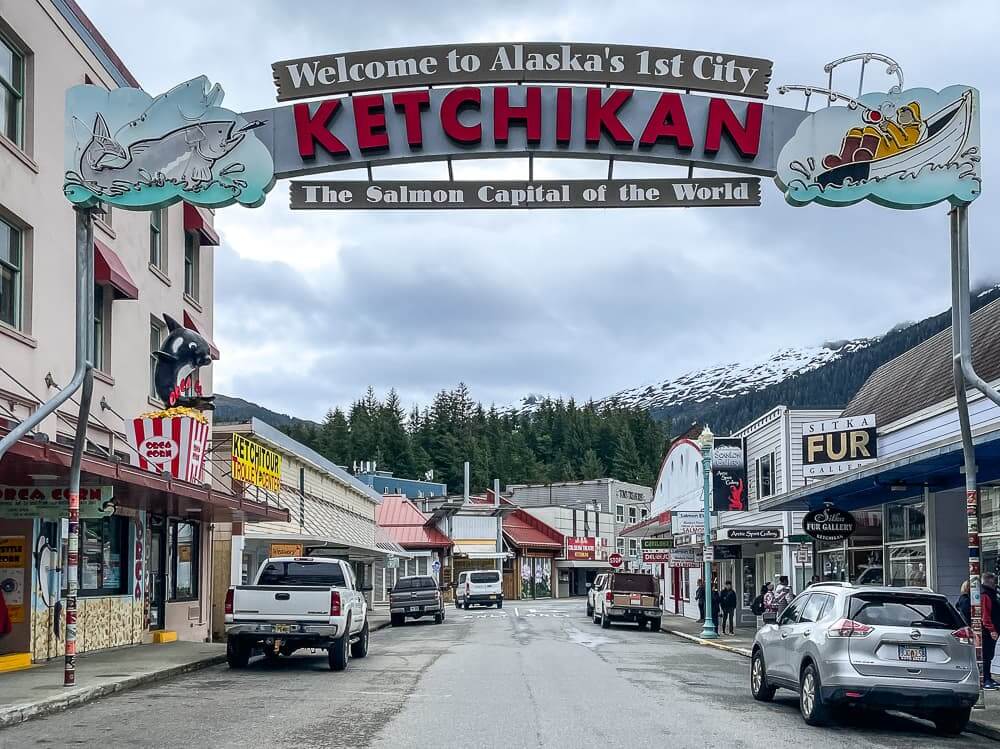 A sign with KETCHIKAN in red letters spans over a street with parked cars.