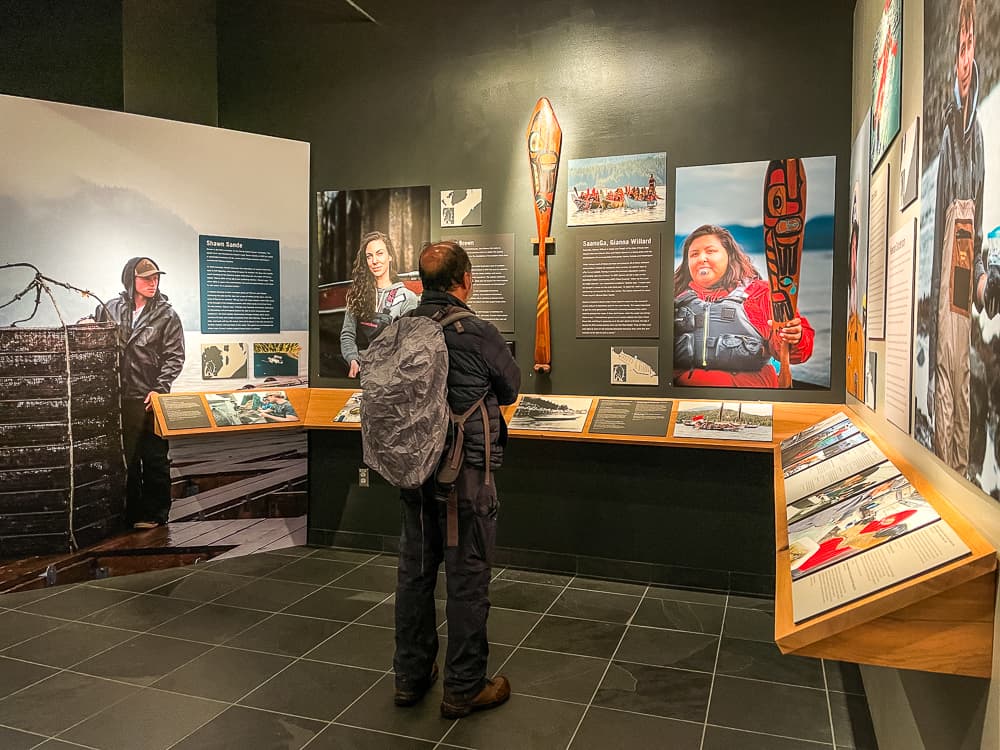 A mean wearing a grey backpack looks at exhibit pictures on the wall.