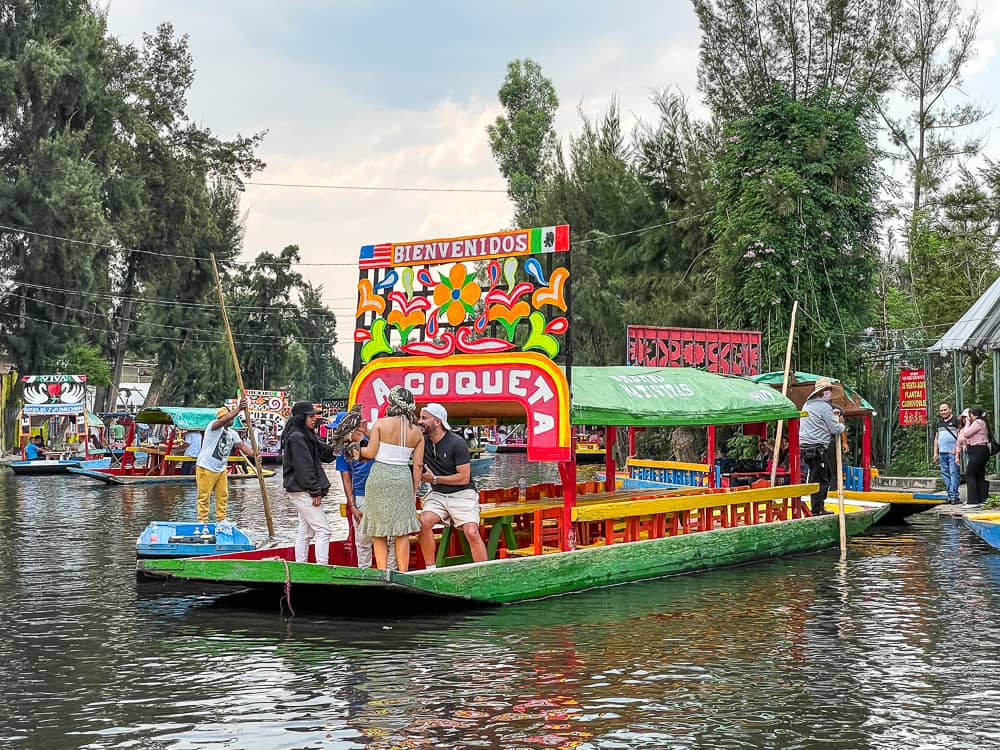 A colorfully decorated, roofed flat-bottomed boat with a red arch with white lettering floats on the water.