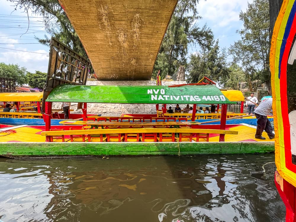 A small flat-bottomed boat painted in yellow, green and red floats under a bridge.