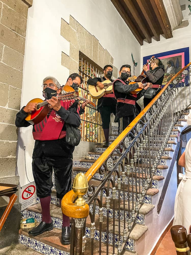 A group of musicians dressed in black and red and holding string instruments stand on a tiled stairway.