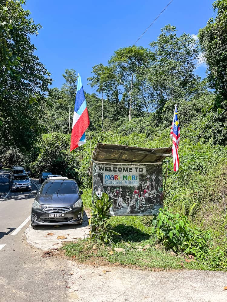 Cars parked next to a wooden sign with two red, white and blue flags flying at either corner.