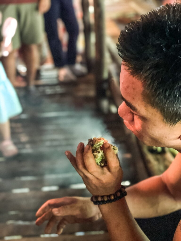 A close up of man blowing on a small smoking piece of moss that he holds in his hands.