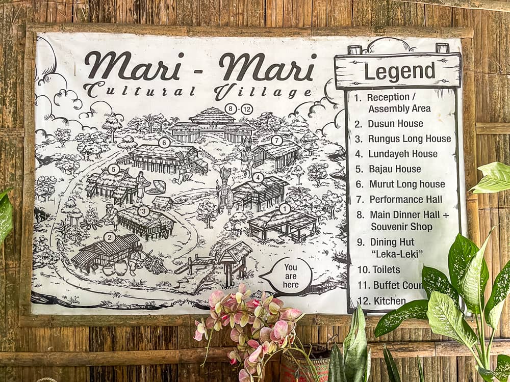 A large black and white sign with Mari- Mari Culture Village at the top, a hand-drawn map, and a legend on the right.