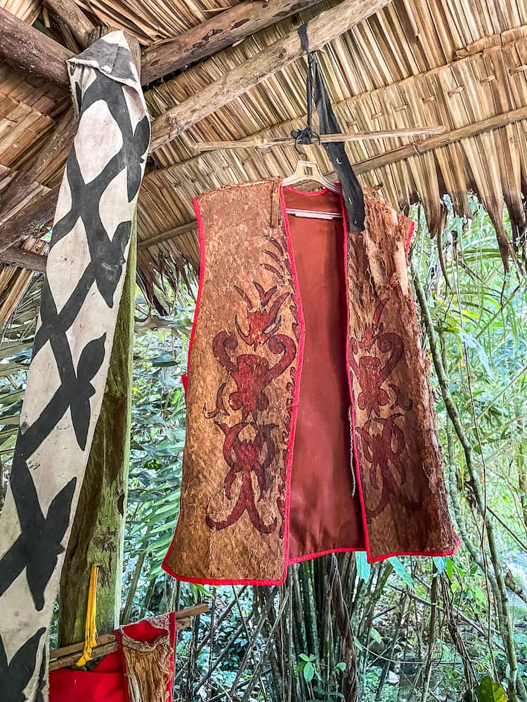 A red decorated vest hangs in a house made of reeds and grasses.