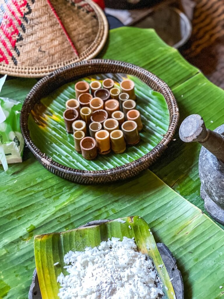 A round tray filled with tiny bamboo bowls sits on a large leaf on a table. 