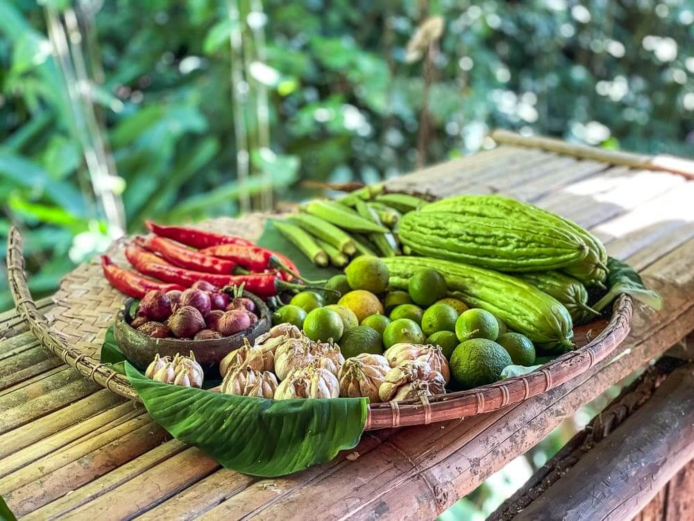 A large woven platter holds colorful vegetables, including peppers, onions, garlic and okra. 