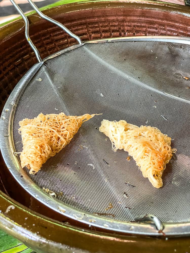 Two triangular fried snacks sit on a circular metal mesh