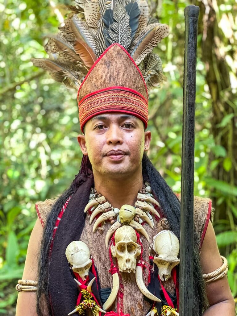 Portrait of a man wearing a feathered headdress and a necklace made of animal bones. 