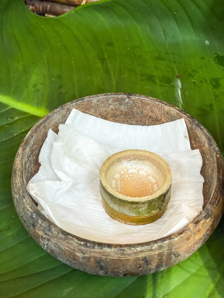 A small bamboo cup sits on a napkin in a wooden bowl, which sits on a bright green leaf. 